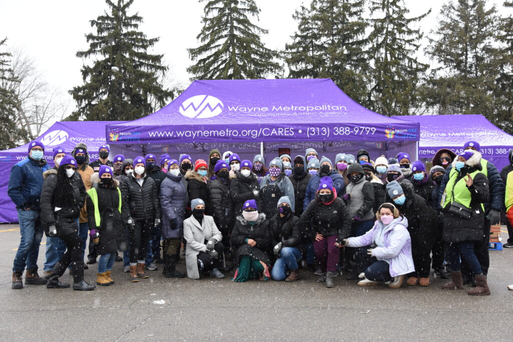 At a distribution drive in Dearborn Heights, Wayne Metro Staff and volunteers pose in front of distribution tents designed and supplied by GM to protect them from the elements