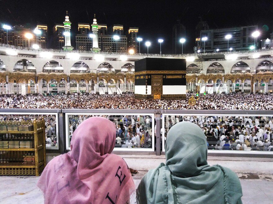 Two women look on as pilgrims surround the Kaaba, in the Grand Mosque, during Hajj 
