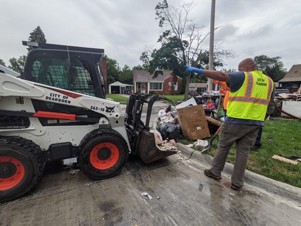 Dearborn employees use a "bobcat" to haul flood debris