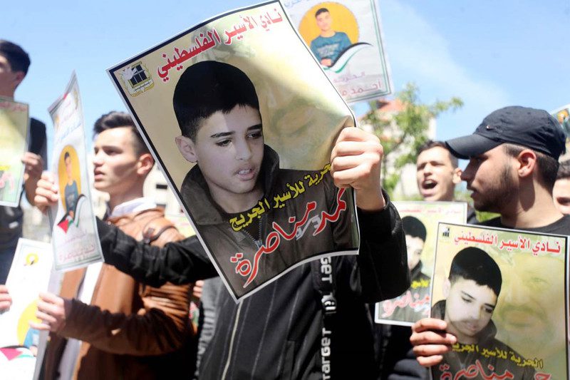 Palestinians hold placards during a protest in solidarity with prisoner Ahmed Manasra who accused of taking part in the stabbing of two Israelis, in front of Red Cross office in the West Bank city of Hebron on April 13. Photo: Samar Bader/WAFA